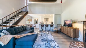 A spacious living area with a dark blue sofa, a coffee table, and a TV. A staircase leads to an upper level. - Cozy lofted condo in Kings Beach close to everything! (Kings Beach)