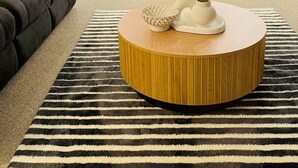 Ein modernes Wohnzimmer mit einem dunkelbraunen Sofa, einem runden Couchtisch aus Holz und einem Streifen Teppich.