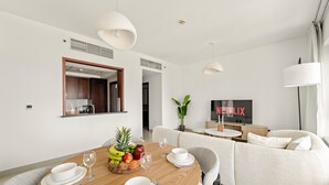 A modern living room with a dining area, white furniture, a TV, and a plant. - 29 Boulevard T2- 2404 1BD (Dubai)
