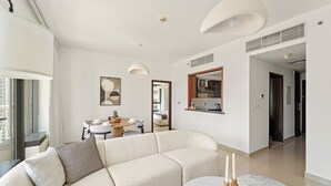 A modern living room with a sofa, a dining table with chairs, a kitchen area, and a view of the city. - 29 Boulevard T2- 2404 1BD (Dubai)