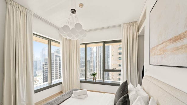 A modern hotel room with a large bed, two windows with curtains, a hanging light fixture, and a city view. - 29 Boulevard T2- 2404 1BD (Dubai)