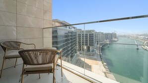 A balcony with two wicker chairs, a glass railing, and a view of a river with a bridge and high-rise buildings. - Canal Front Building 9 A - 1001 2BD (Dubai)