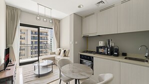 Eine moderne Küche mit Gasherd, Kaffeemaschine und Spüle. Ein Essbereich mit rundem Tisch und Stühlen ist ebenfalls vorhanden. Das Zimmer verfügt über große Fenster mit Blick auf ein Gebäude.