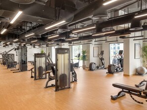 Une salle de sport équipée de divers appareils d’exercice, dotée de planchers en bois et de grandes fenêtres laissant entrer la lumière naturelle.
