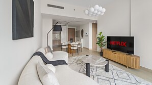 A modern living room with a sofa, a coffee table, a TV, and a dining area in the background. - Azizi Riviera 3 - 804 1BD (Dubai)