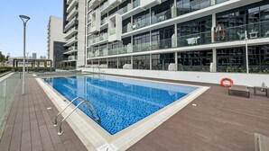 A modern building with a swimming pool, outdoor seating, and a clear sky. - Azizi Riviera 3 - 804 1BD (Dubai)
