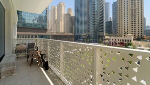 Ein Balkon mit Blick auf hohe Gebäude, eine Sitzecke mit Sofa und Tisch sowie ein dekorativer weißer Zaun.