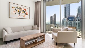 Una sala moderna con sofá, sillón y mesa de centro, un cuadro abstracto grande, y vista a la ciudad a través de amplios ventanales.