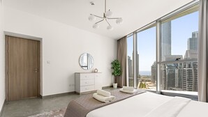 Una habitación de hotel moderna con una cama grande, un espejo redondo, un escritorio pequeño y vistas de la ciudad a través de amplios ventanales.