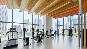 Un gimnasio moderno con diversos equipos de ejercicio, grandes ventanales que ofrecen vistas a la ciudad y techo de madera.