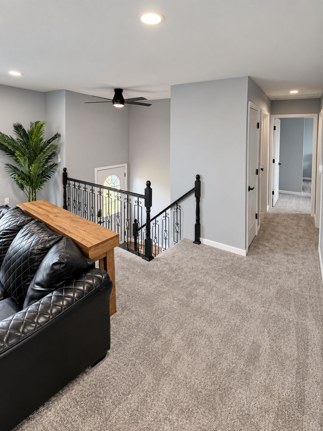 A staircase with a black railing, a wooden table, and a black leather sofa in a room with light grey walls and carpet.