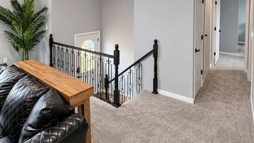 A staircase with a black railing, a wooden table, and a black leather sofa in a room with light grey walls and carpet.