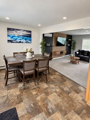 A modern living space with a dining area, a flat-screen TV mounted on a wall, and a black leather sofa. - Charming 4-bedroom house. NO ANIMALS. (Wolf Point)