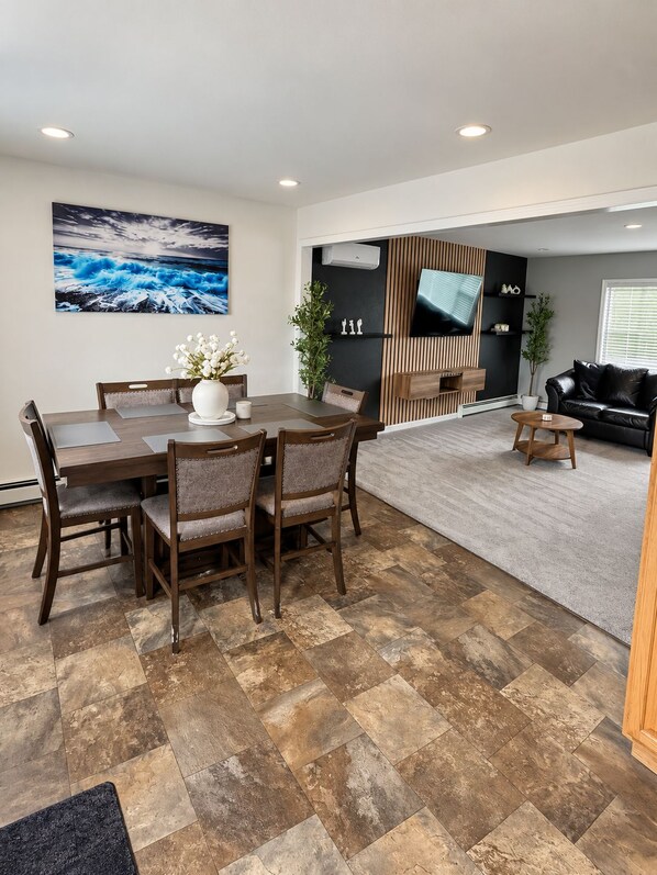 A modern living space with a dining area, a flat-screen TV mounted on a wall, and a black leather sofa.