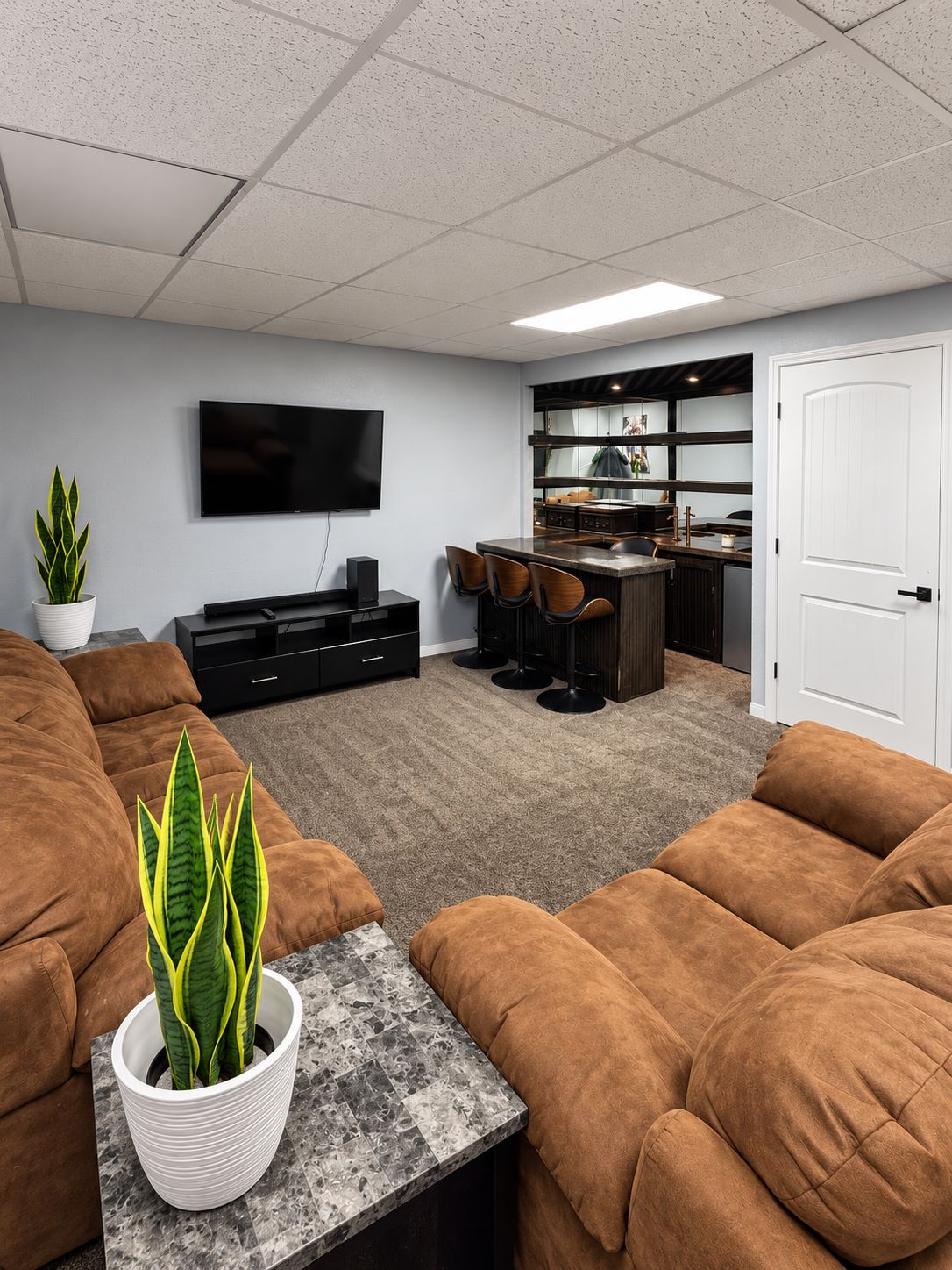 A modern living room with a flat-screen TV, brown sofas, a coffee table, and a potted plant.