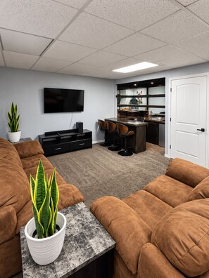 A modern living room with a flat-screen TV, brown sofas, a coffee table, and a potted plant.