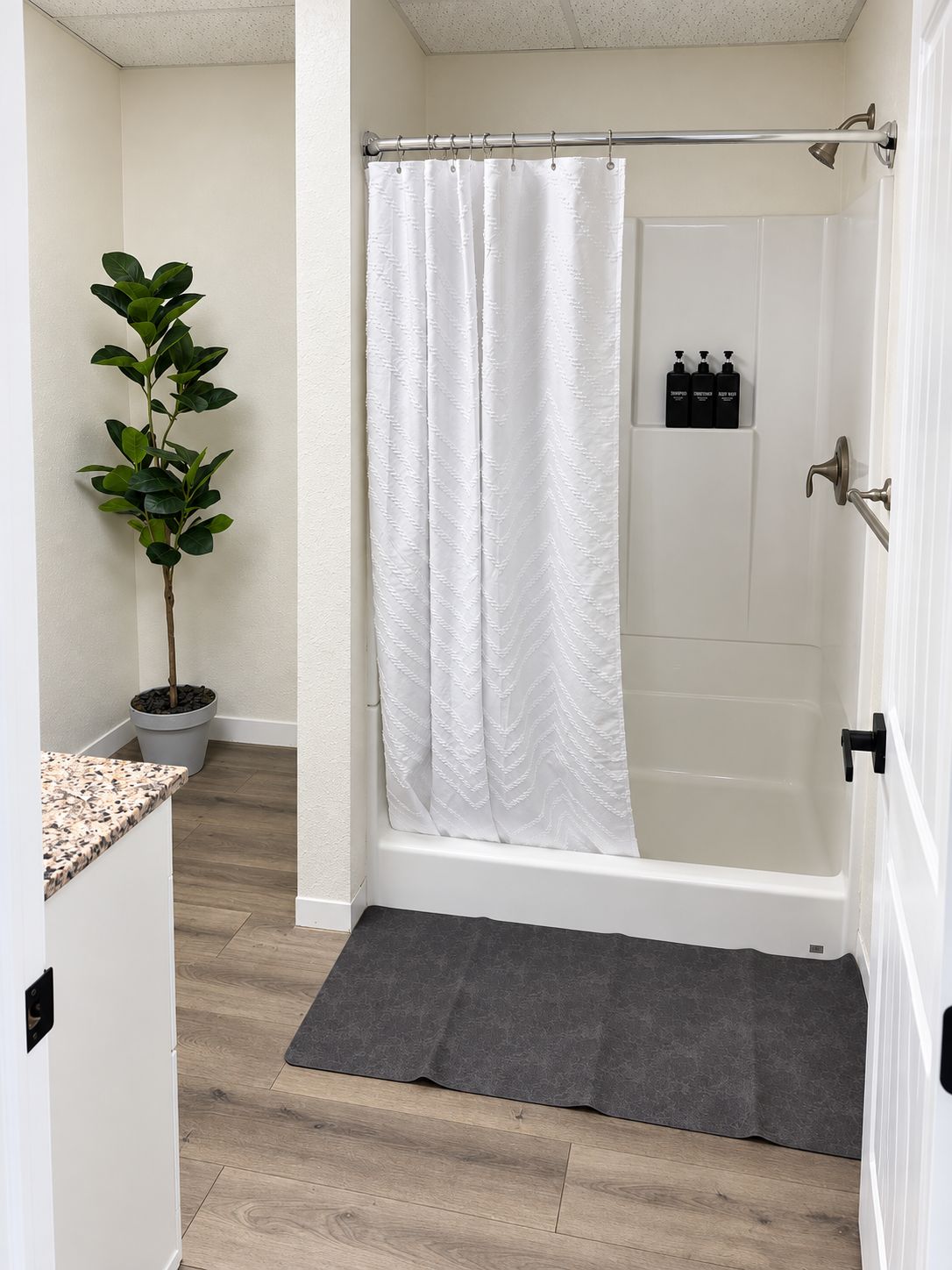 Un baño con cortina de ducha, una planta en maceta y artículos de tocador en la pared.