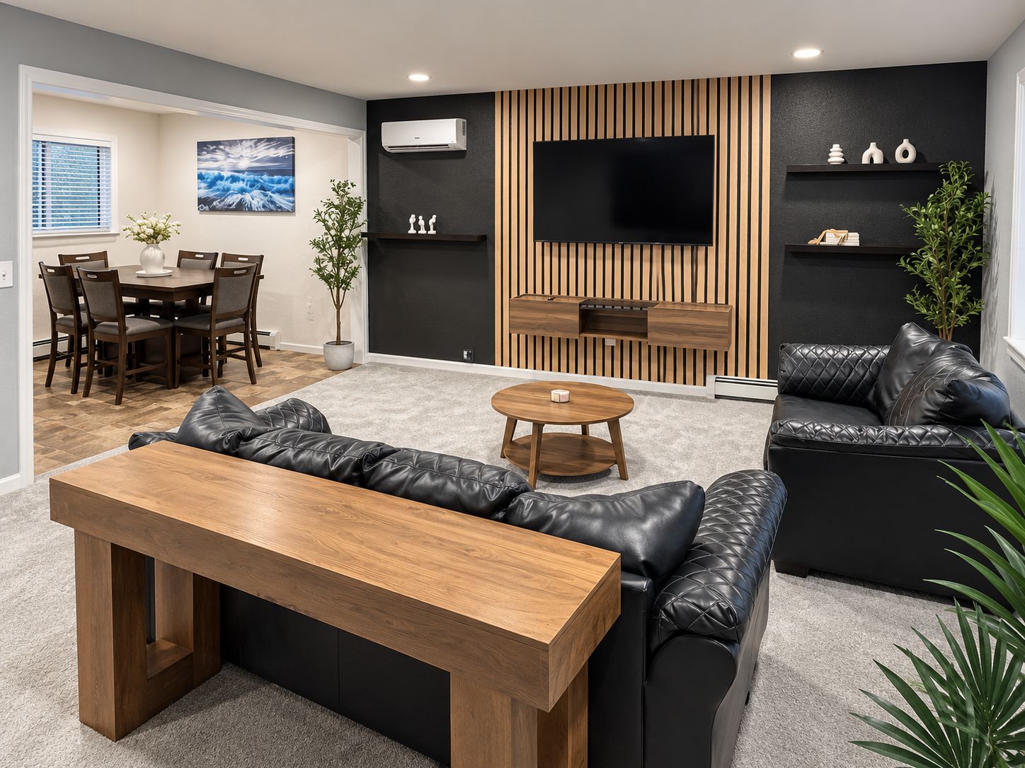 A modern living room with a wooden coffee table, black leather sofa, and a flat-screen TV mounted on a wooden panel wall.