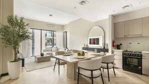 A modern kitchen with a large island, a dining area with chairs, a potted plant, and a large window. - Act Two Tower - 1902 2BD (Dubai)