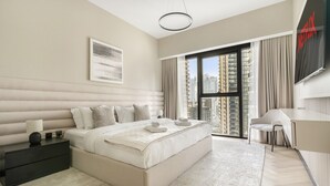 A modern bedroom with a large bed, a nightstand, a desk, and a view of the city through a large window. - Act Two Tower - 1902 2BD (Dubai)