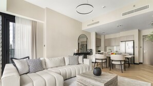 A modern living room with a sofa, coffee table, and dining area. - Act Two Tower - 1902 2BD (Dubai)