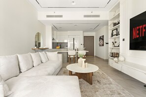 A modern living room with a sectional sofa, a round coffee table, and a TV on the wall. - Act Two Tower - 3402 2BD (Dubai)