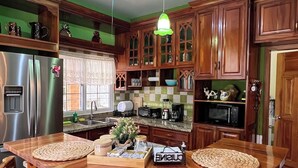 Une cuisine avec des meubles de rangement en bois, un îlot central doté de chaises, un ventilateur de plafond et des luminaires suspendus.