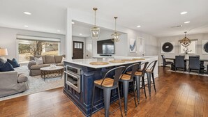 A modern kitchen with a central island, bar stools, and a dining area with a table and chairs. - Nautical, Pet-Friendly | Walk to Lake & Downtown (Lake Geneva)