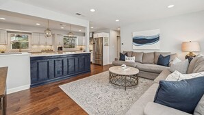A modern kitchen with a central island, a dining area with a round table, and a living room with a sofa and a rug. - Nautical, Pet-Friendly | Walk to Lake & Downtown (Lake Geneva)
