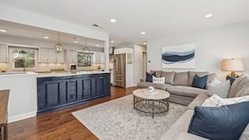 A modern kitchen with a central island, a dining area with a round table, and a living room with a sofa and a rug.