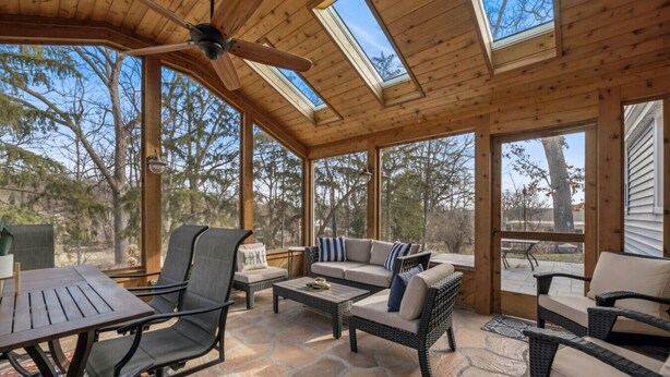 A covered patio with wicker furniture, a ceiling fan, and large windows offering views of trees. - Nautical, Pet-Friendly | Walk to Lake & Downtown (Lake Geneva)