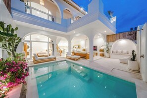 Un espace piscine intérieur luxueux, doté de nombreux coins salon et d’un escalier menant à un niveau supérieur.
