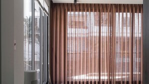 Une pièce spacieuse avec de grandes fenêtres, un radiateur et une vue sur un bâtiment à l’extérieur.
