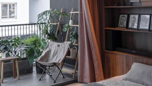 Un salon moderne doté d’une grande fenêtre, d’un balcon agrémenté de plantes, d’une bibliothèque en bois et d’un coin salon confortable.