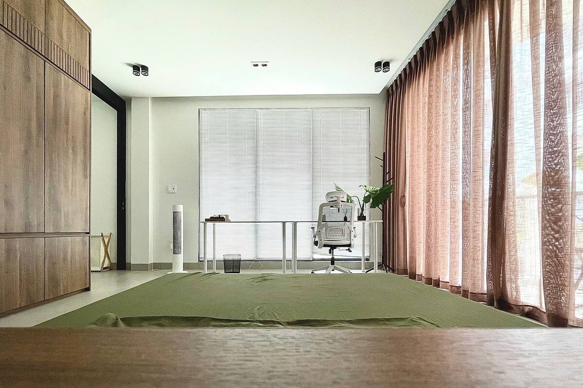 A spacious room with a large window, a standing desk, and a green carpet.