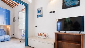 Een moderne woonkamer met een bank, een televisie op een houten dressoir en een blauw omlijste deur naar een andere kamer.