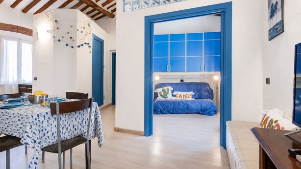 Een kamer met een bed, een tafel met stoelen, een blauwe deur en een raam met kunstwerk.