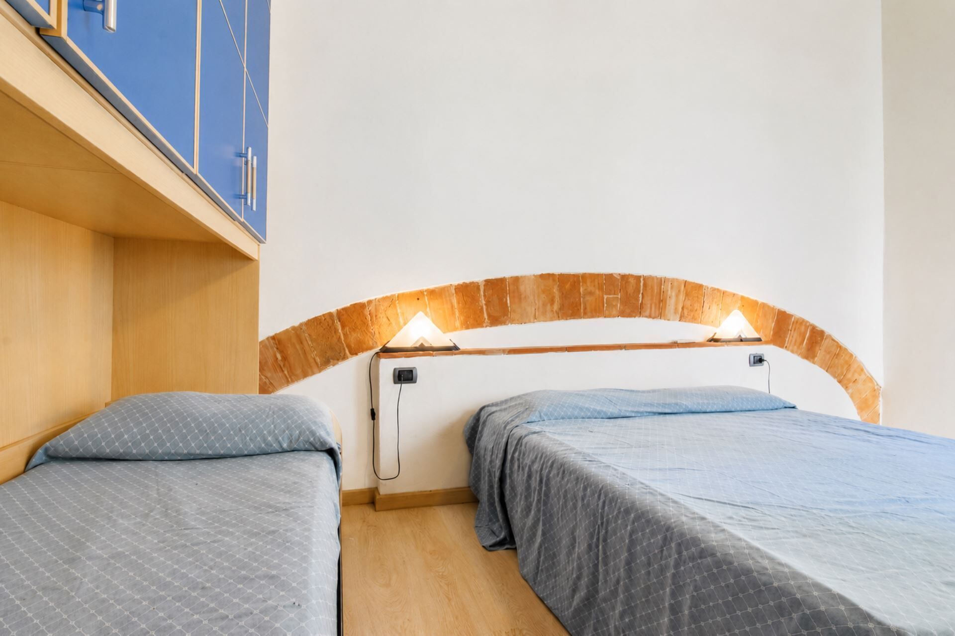 A room with two beds, wooden headboard, and a blue cabinet.