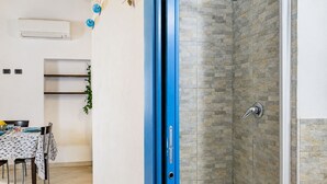 Een kamer met een douche, een tafel met stoelen en een wandairconditioner.