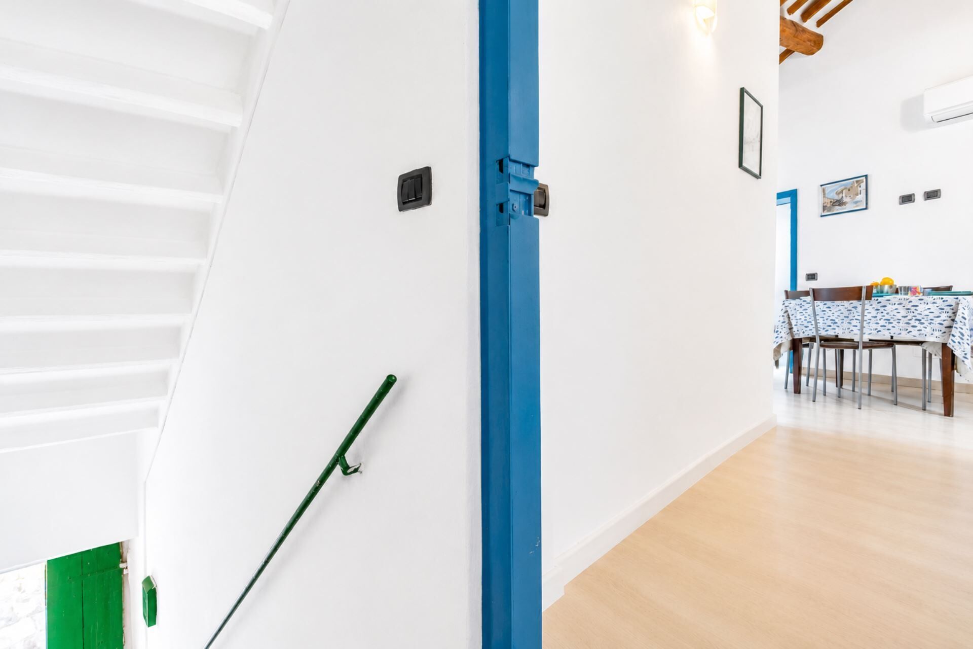 A hallway with a blue door, a green broom, and a dining area with a table and chairs.