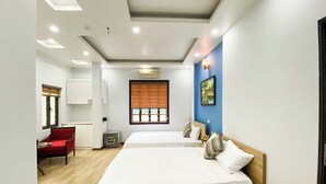 Ein Hotelzimmer mit zwei Betten, einem roten Sessel, einem kleinen Tisch und einem Fenster mit Jalousien.