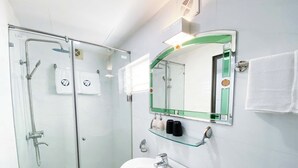 Ein modernes Badezimmer mit einer Duschkabine aus Glas, einem weißen Waschbecken und einem Spiegel mit grünem Rahmen.