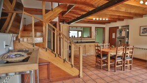 A spacious kitchen with wooden flooring, a dining area with a table and chairs, and a staircase with wooden railings.
