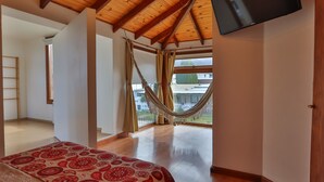 A bedroom with a large bed, wooden ceiling beams, a hammock, and a TV mounted on the wall.