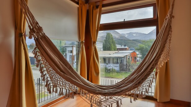 A hammock in a room with large windows overlooking a residential area and mountains.