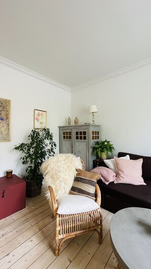 Un salon avec un fauteuil en osier, un canapé foncé, un buffet rouge et une table grise.