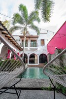 Un patio con piscina, palmeras y un edificio con puertas arqueadas.