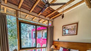 A bedroom with a bed, a chair, a nightstand, a ceiling fan, and a window with a view of buildings outside. - Los Suspiros Hotel Boutique & Spa (Comala)