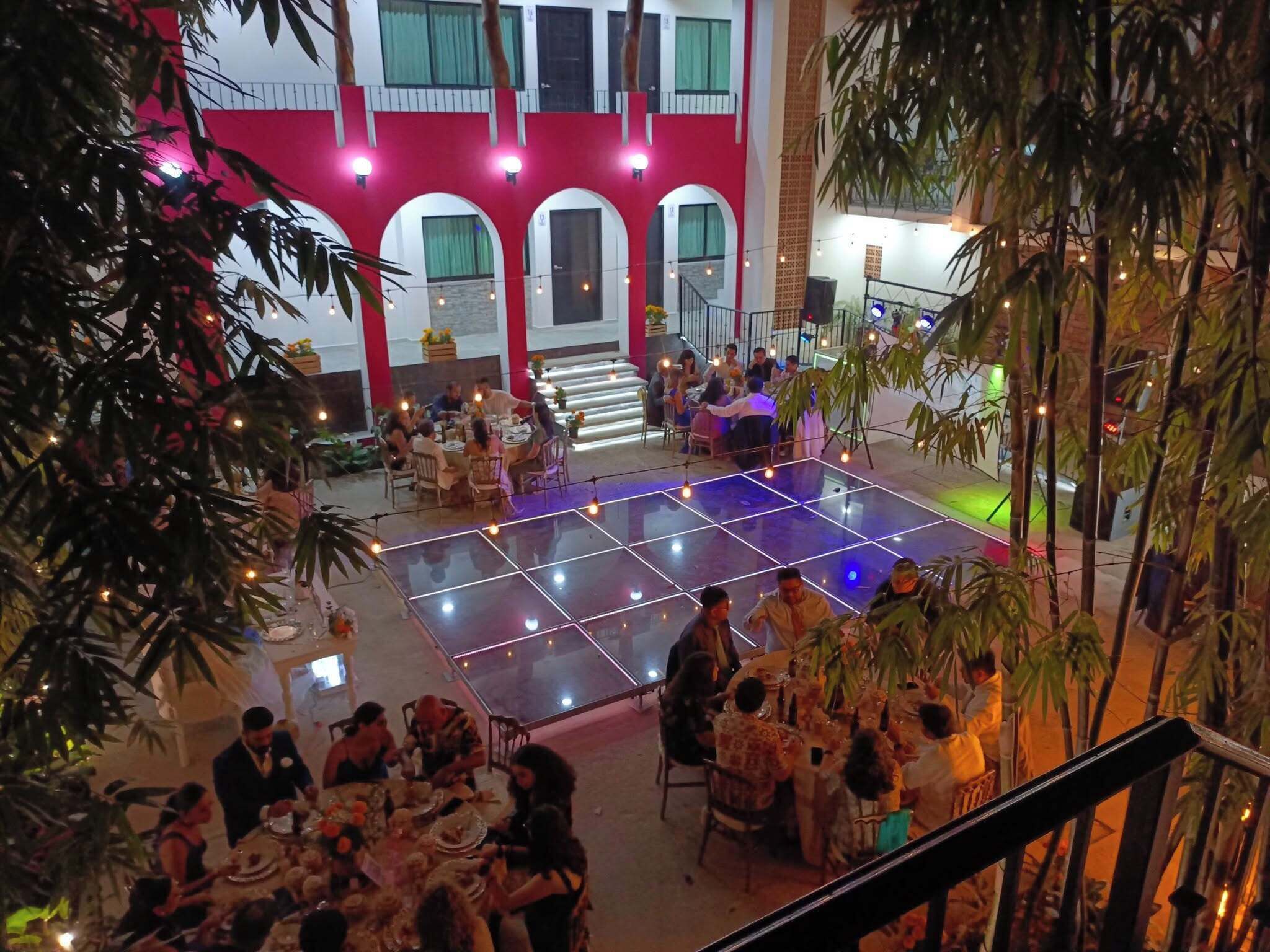 Un espacio interior para comer con mesas dispuestas alrededor de una pista de baile central, rodeado por un edificio de color rojo y blanco con ventanas arqueadas.