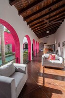 Un amplio espacio exterior con terraza techada, sofás blancos y una piscina.